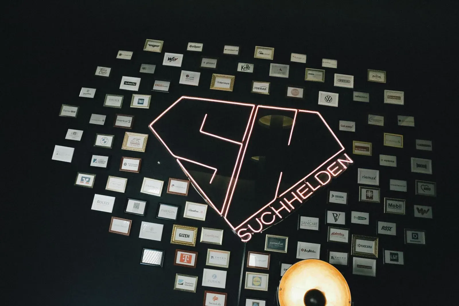 Kundenwand mit gerahmten Logos rund um das SH-Neonlogo im Suchhelden-Büro in Osnabrück Kundenwand mit gerahmten Logos rund um das SH-Neonlogo im Suchhelden-Büro in Osnabrück