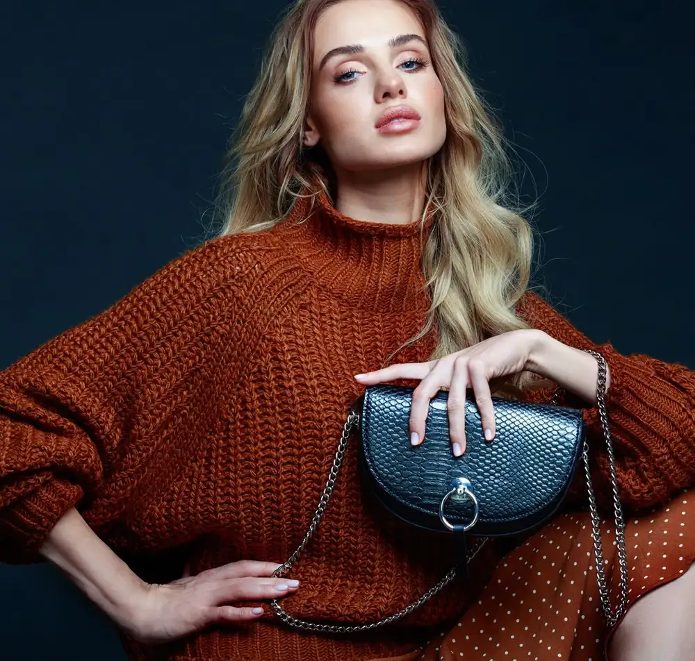 Portraet einer blonden jungen Frau mit langen Haaren, die braunen Pullover und Rock traegt Portraet einer blonden jungen Frau mit langen Haaren, die braunen Pullover und Rock traegt