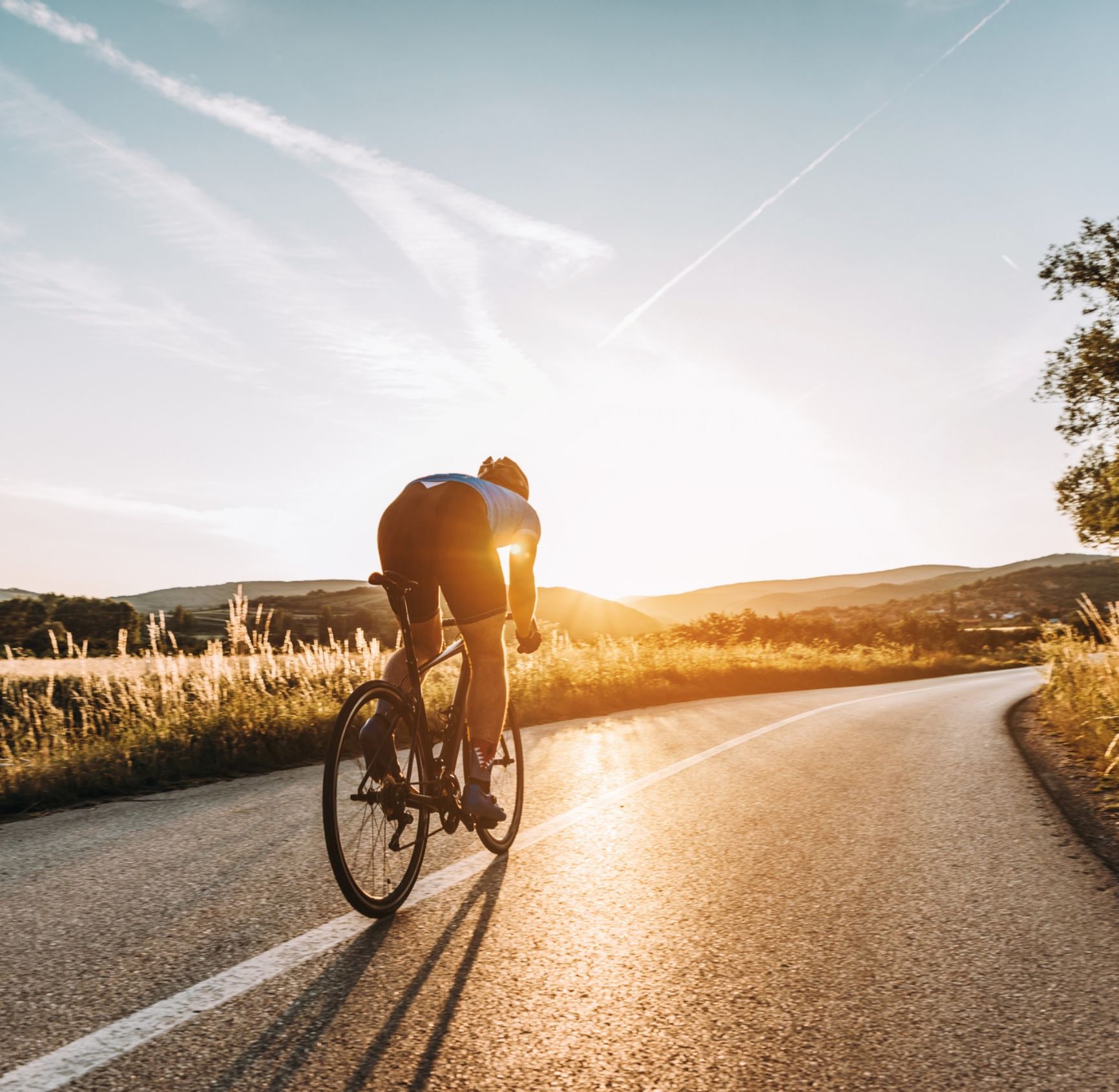Radfahrer-Silhouette bei Sonnenuntergang auf Landstraße von bike und co