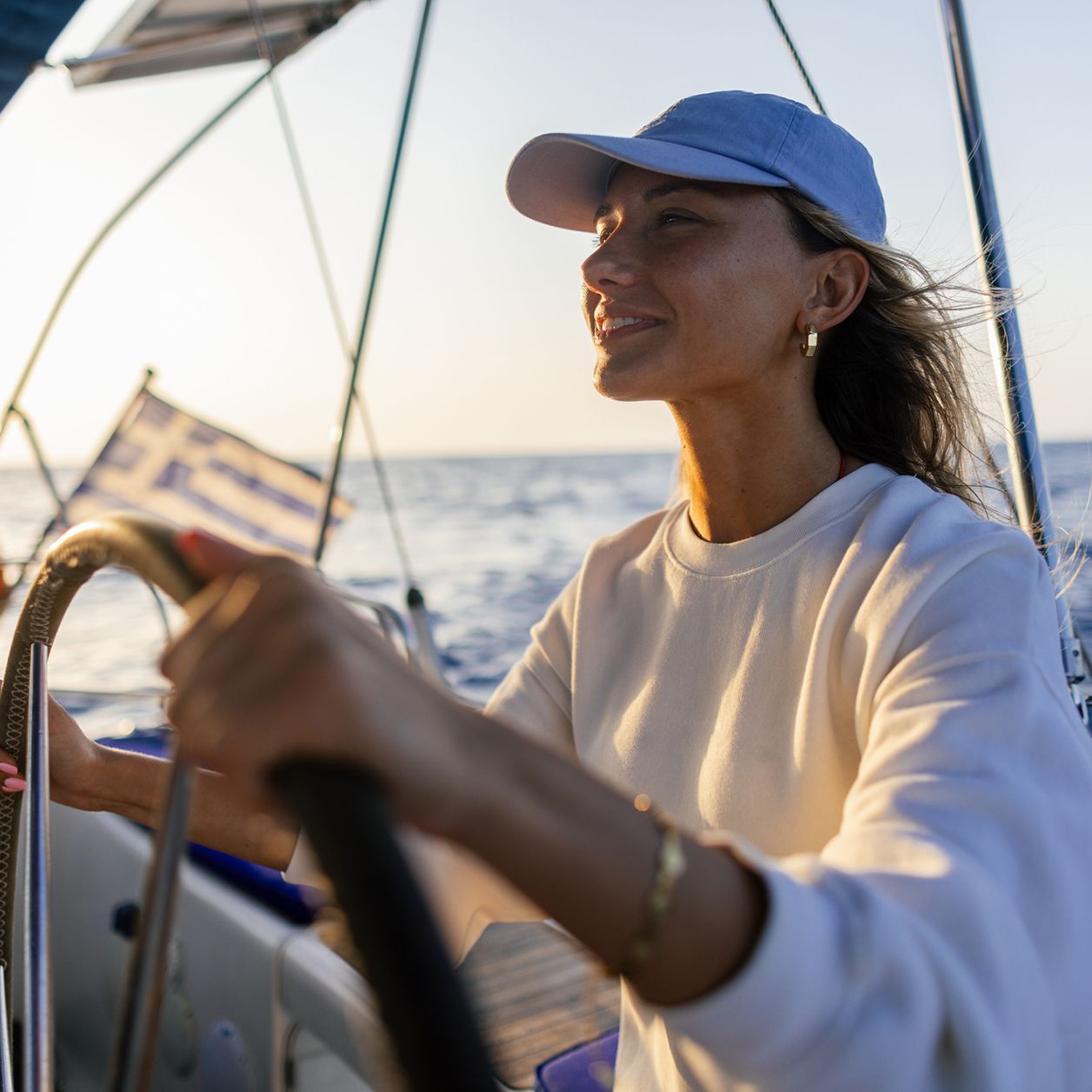 Frau in weissem Jackett am Steuerrad eines Segelbootes von 1ayachtcharter