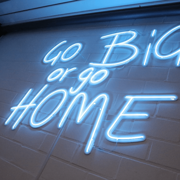 Leuchtstoffröhre an Wand zeigt Text "Go Big or Go Home" in modernem Büroumfeld