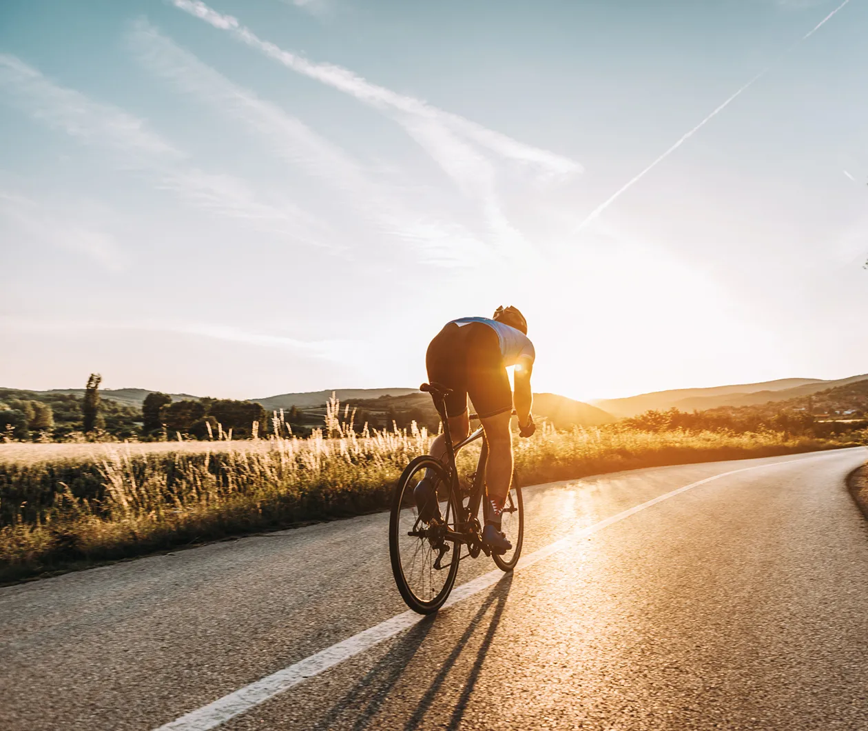 Fahrradfahrer faehrt auf einer leeren Strasse bei Sonnenuntergang