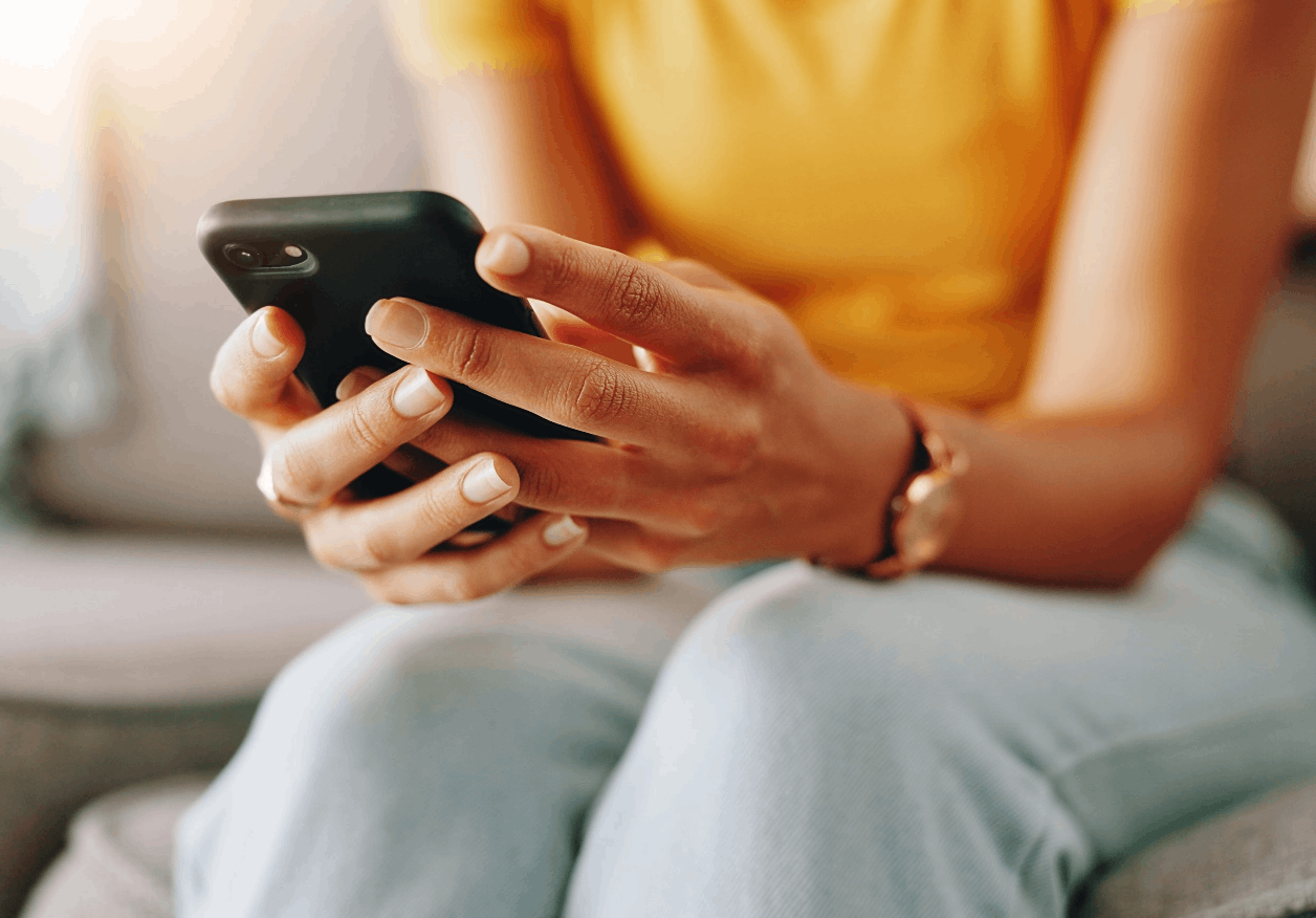 Eine Frau hält sitzend ihr Smartphone in beiden Händen.