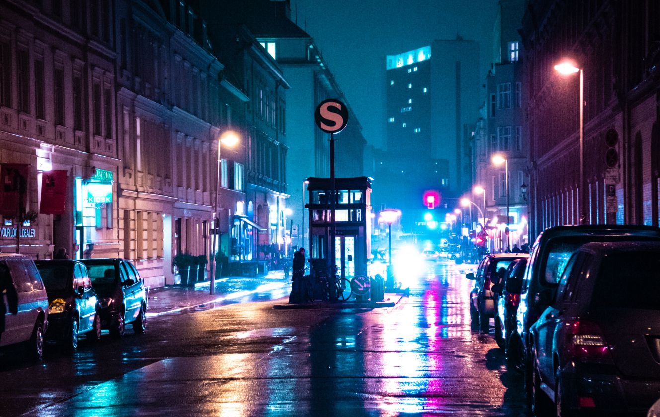 Eine beleuchtete Stadtstrasse bei Nacht, mit bunten Lichtern und geparkten Autos
