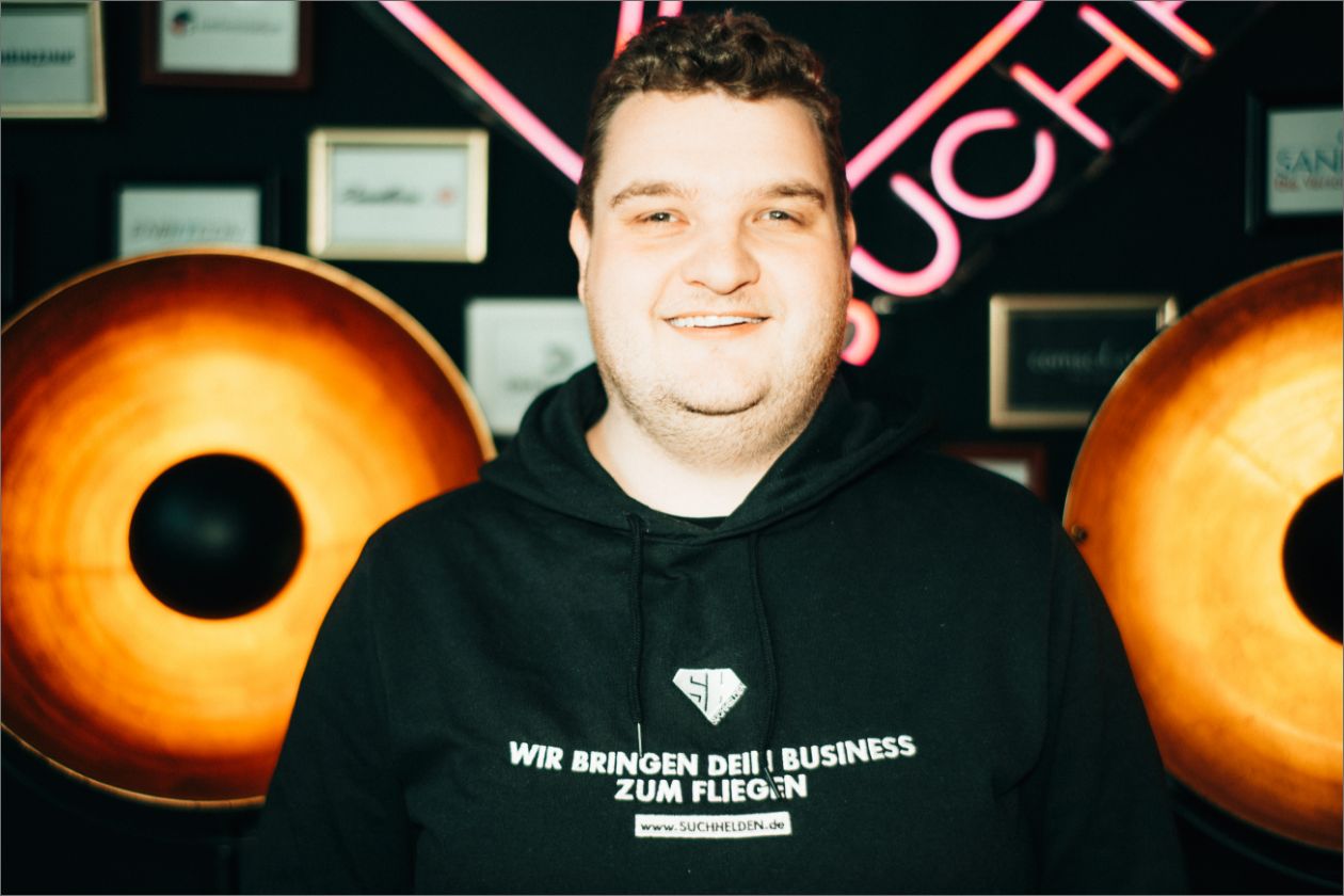 Florian Meyer lächelt, trägt Hoodie mit Aufschrift, in warmer Beleuchtung.