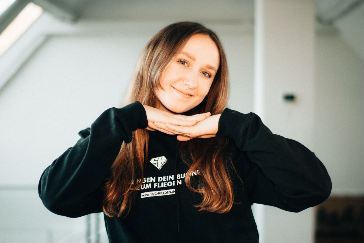 Hannah Bade lächelt und trägt schwarzen Hoodie mit SUCHHELDEN - Schriftzug.