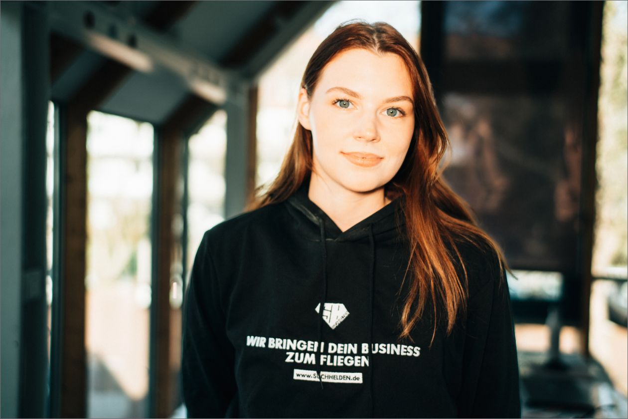 Jördis Meeske in Kapuzenpullover steht in einem modernen, lichtdurchfluteten Raum.