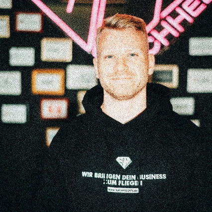 Leon Westerheide lächelt vor einer Wand mit Zertifikaten und Suchhelden-Logo.