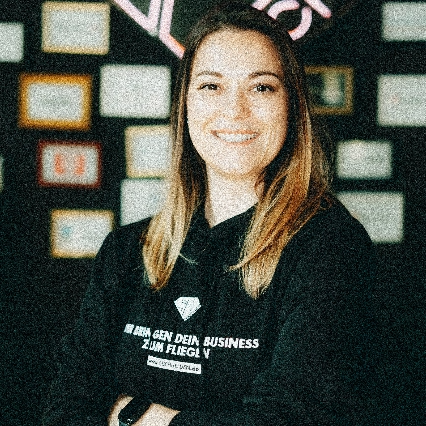 Tessa Egbert lächelt im schwarzen Hoodie vor einer Wand mit Bildern.