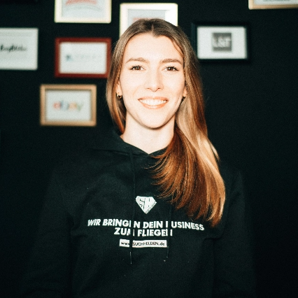 Liesa Marie Bockholt in einem schwarzen Pullover vor einer Wand mit Logos